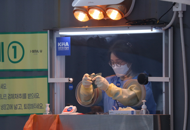 24일 오전 서울광장에 마련된 임시선별진료소에서 한 의료진이 핫팩으로 손을 녹이고 있다./연합뉴스