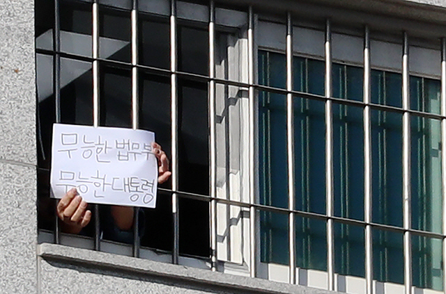 6일 오후 서울 송파구 동부구치소에서 한 수용자가 ‘무능한 법무부 무능한 대통령’이라고 쓴 종이를 창문 밖 취재진에게 내보이고 있다. /연합뉴스