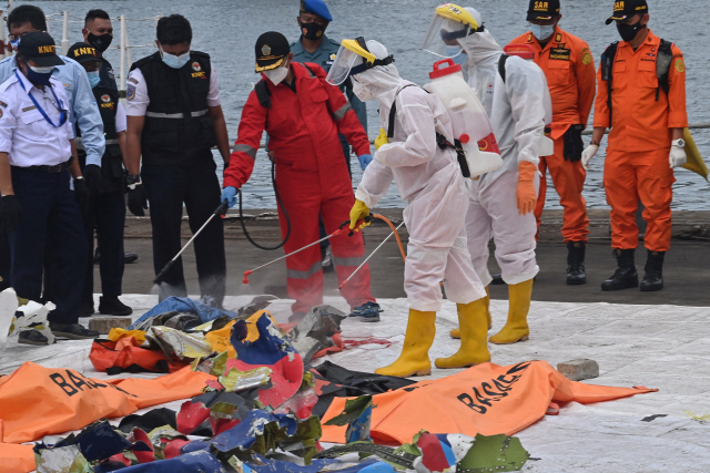 인도네시아 적십자사 관계자들이 추락한 비행기 잔해에 12일(현지시간) 소독약을 뿌리고 있다. /AFP연합뉴스