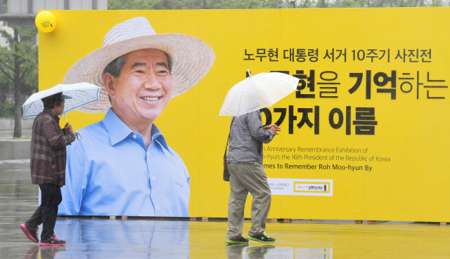 노무현 전 대통령 서거 10주기를 나흘 앞둔 19일 서울 광화문광장에 노 전 대통령의 사진 전시회가 열리는 가운데 우산을 쓴 시민들이 사진 앞을 지나가고 있다./권욱기자 2019.05.19