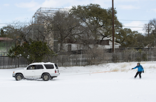 Ehsan M. rides a snowboard behind a friend\'s SUV in a parking lot in Travis Heights after a heavy snow on Monday Feb. 15, 2021. (Jay Janner /Austin American-Statesman via AP) MANDATORY CREDIT; AUSTIN CHRONICLE OUT; COMMUNITY IMPACT OUT; WEBSITES AND TV MUST CREDIT PHOTOGRAPHER AND STATESMAN.COM; NO LICENSING EXCEPT BY AP COOPERATIVE MEMBERS