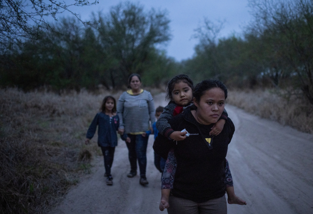 온두라스에서 온 타스나리가 3살 아이를 업고 미국 텍사스주의 국경지대 페니타스의 흙길을 16일(현지시간)걷고 있다. 이들은 뗏목을 타고 리오그란데 강을 건넜다./로이터연합뉴스