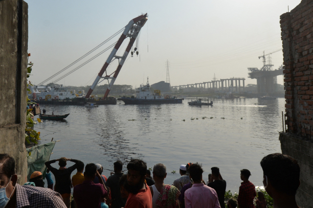 방글라데시 수도 다카 남쪽에 있는 나라양간지의 시탈라크키아 강에서 5일(현지시간) 구조선이 크레인을 이용해 전복 선박 인양작업을 벌이고 있다. 인근 강둑에서는 주민과 실종자 가족들이 이 모습을 지켜보고 있다. /AFP연합뉴스
