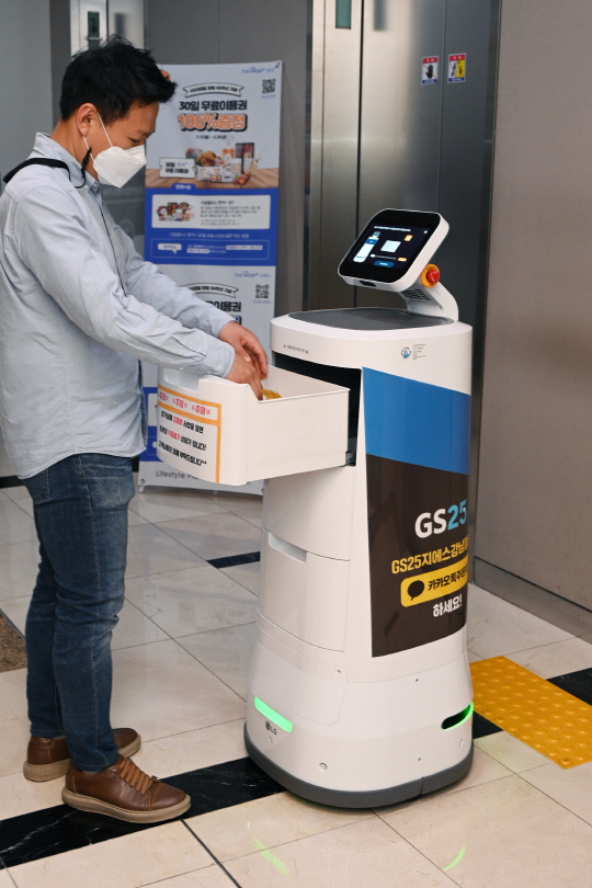 한 직장인이 서울 강남구 역삼동 GS타워에서 실내 로봇 'LG 클로이 서브봇(LG CLOi ServeBot)’이 배송한 물품을 받고 있다. /사진 제공=LG전자