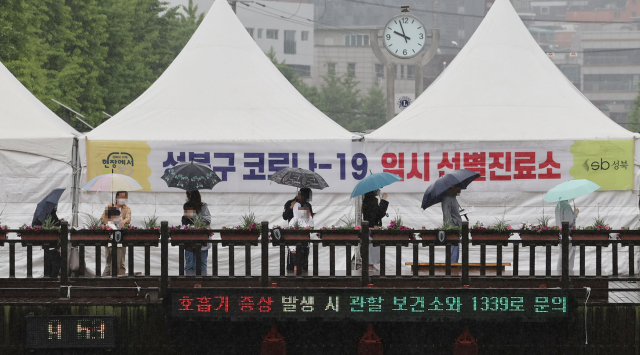 지난 16일 오전 서울 성북구청 앞에 설치된 임시선별진료소에서 시민들이 우산을 쓰고 검사를 위해 대기해 있다./연합뉴스