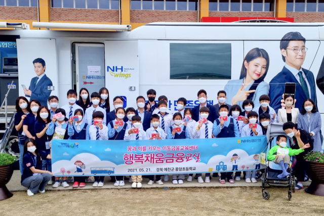 NH농협은행 임직원들과 N돌핀 대학생봉사단이 지난 21일 경북 예천군 풍양초등학교에서 풍양초등학교 학생들에게 이동금융교육을 실시한 뒤 개설한 통장을 들고 있다./사진 제공=농협은행