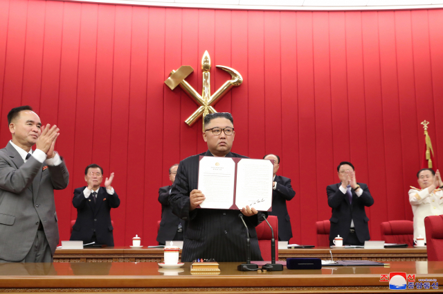 김정은 총비서가 자신의 서명이 기재된 서류를 들어보이고, 간부들이 박수를 치고 있다./연합뉴스