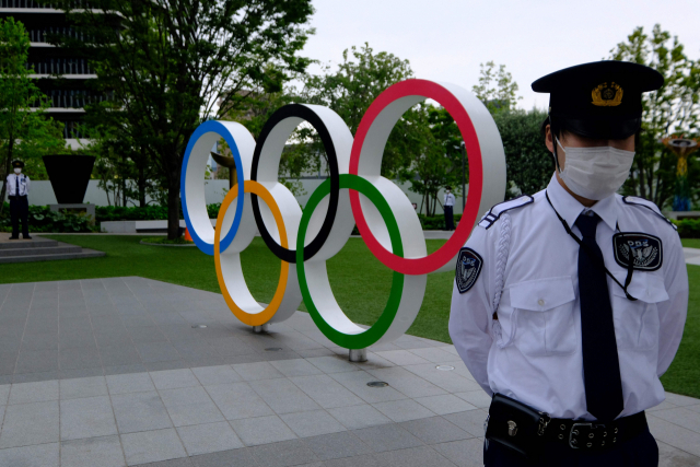 지난달 18일 도쿄올림픽 개최 반대 시위가 벌어진 도쿄의 일본올림픽조직위원회 본부 앞 올림픽 조형물 앞에서 경비원이 경계를 서고 있는 모습. /연합뉴스