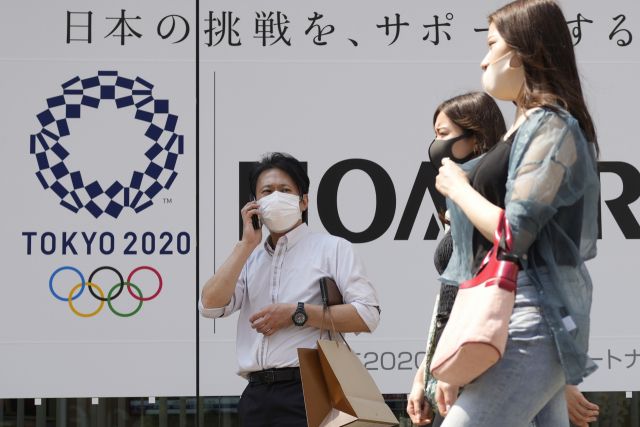 일본 도쿄에서 지난 25일 코로나19 예방 마스크를 쓴 시민들이 개막이 채 한 달도 남지 않은 도쿄올림픽의 포스터 앞을 지나고 있다./AP연합뉴스