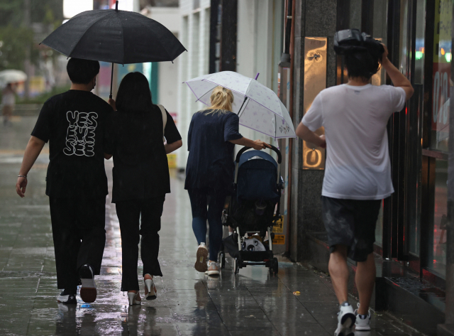 소나기가 내린 지난 27일 오후 서울 보신각 인근 거리에서 한 시민이 우산을 든 채 유모차를 끌고 있다./연합뉴스