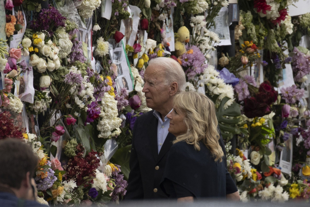 조 바이든 미국 대통령과 그의 부인 질 여사가 1일(현지 시간) 플로리다주 아파트 붕괴 사고 관련 실종자들의 사진과 꽃이 걸려 있는 철제 펜스를 둘러보고 있다./AFP연합뉴스