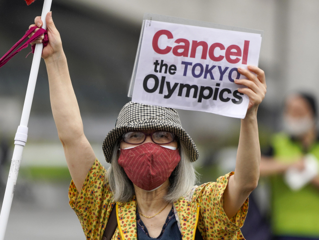 지난 9일 도쿄올림픽 성화 도착 행사가 열린 일본 도쿄의 고마자와 올림픽공원 체육관 앞에서 한 여성이 피켓을 든 채 올림픽 개최 반대 시위를 벌이고 있다./도쿄=EPA연합뉴스