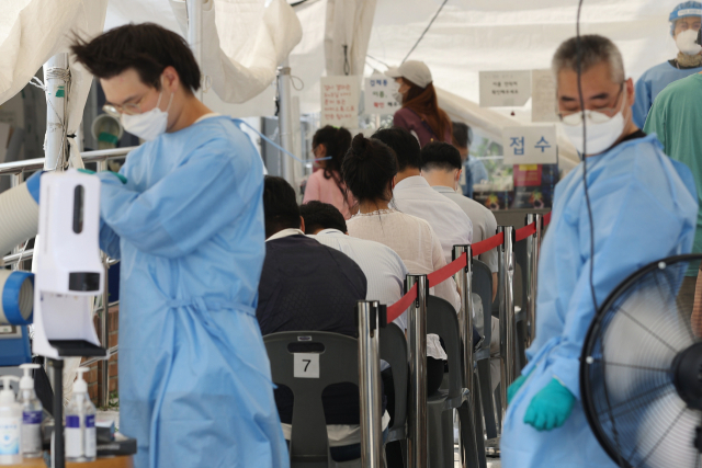 15일 오후 서울 영등포구 도림동 배드민턴 체육관 임시 선별 검사소에서 더위를 식히는 의료진 뒤로 검사를 받기 위해 시민들이 대기하고 있다. /연합뉴스