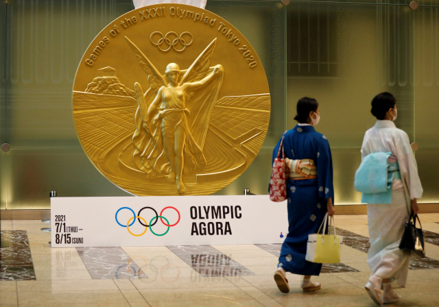 도쿄 올림픽·패럴림픽 개막을 앞둔 지난 14일 일본 수도 도쿄의 니혼바시 미쓰이 타워에 설치된 대형 올림픽 메달 모형 앞을 전통 복장에 신종 코로나바이러스 감염증(코로나19) 예방 마스크를 쓴 여성들이 걸어가고 있다./로이터연합뉴스