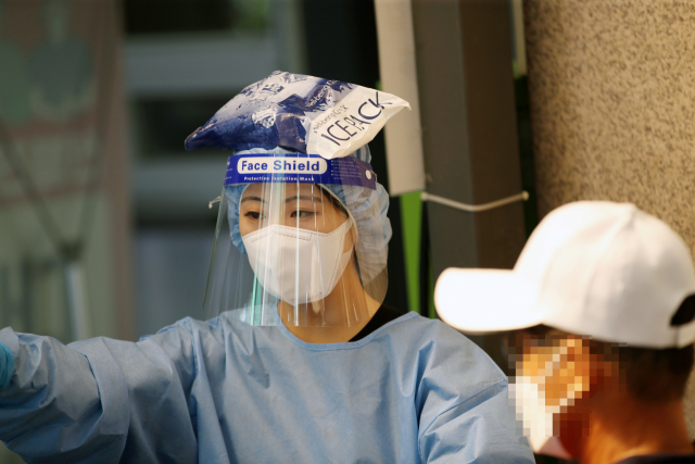 보건소 선별진료소에서 한 의료진이 아이스팩을 머리에 얹고 있다./연합뉴스
