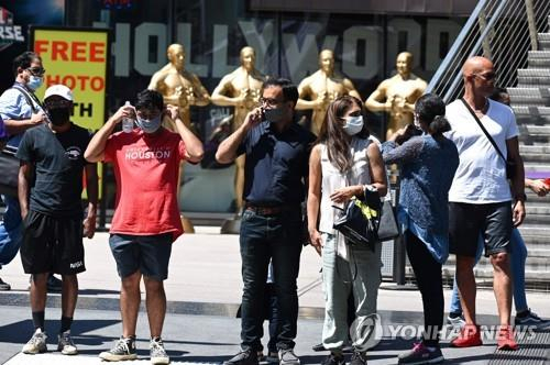 19일(현지시간) 실내 마스크 착용 의무화가 복원된 미 캘리포니아주 LA의 할리우드에서 길을 건너려 신호를 기다리는 사람들이 마스크를 쓴 채 서 있다./AFP연합뉴스