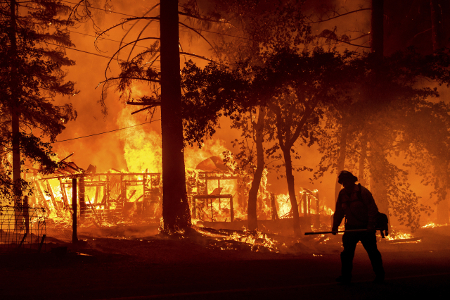 미국 캘리포니아주 플루머스 카운티에서 24일(현지시간) '딕시'란 이름의 대형 산불이 주택을 불태우고 있는 화재 현장을 한 소방관이 지나고 있다. /AP연합뉴스