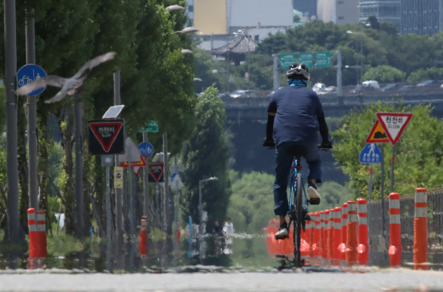 공원을 찾은 시민이 지열로 아지랑이가 피어오르는 자전거도로를 지나고 있다/연합뉴스