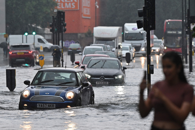 지난 25일(현지시간) 영국 런던에 내린 기록적인 폭우가 내린 가운데 차량들이 물에 잠긴 도로 위를 지나가고 있다./ AFP연합뉴스