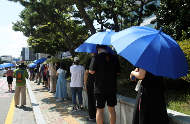 선별진료소에서 시민들이 구청에서 제공한 우산으로 햇볕을 가리고 줄 서 있다./연합뉴스