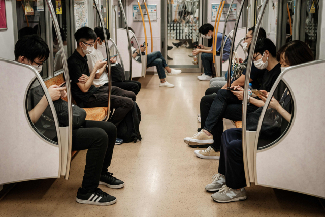 지난달 23일 마스크를 쓴 일본 도쿄 시민들이 열차 안에 앉아 휴대전화를 통해 생중계 되는 도쿄올림픽 개막식을 시청하고 있다. /AFP연합뉴스