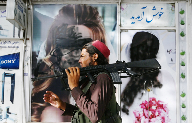 18일(현지 시간) 아프가니스탄 카불에서 무장 탈레반 대원이 스프레이로 흉하게 훼손된 여성 사진이 걸린 미용실 외벽을 지나고 있다. /AFP연합뉴스