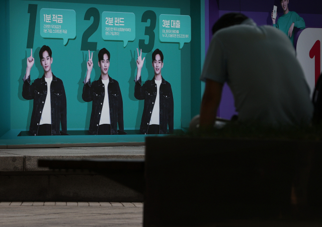 20일 서울시내 한 은행에 내걸린 대출 등 은행 금융상품 광고판 앞에 한 시민이 휴식을 취하고 있다. /연합뉴스