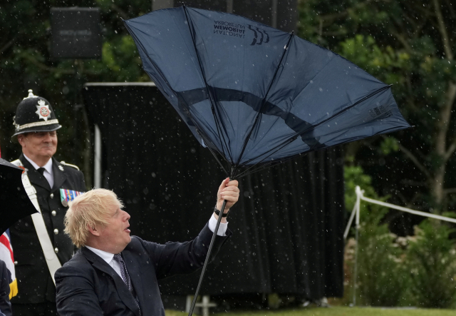 지난 7월 28일(현지시간) 영국 잉글랜드 중서부 스태퍼드셔의 국립기념수목원을 찾은 보리스 존슨 영국 총리가 갑자기 불어온 바람에 쓰고 있던 우산이 뒤집어지자 난감해하고 있다. /로이터연합뉴스