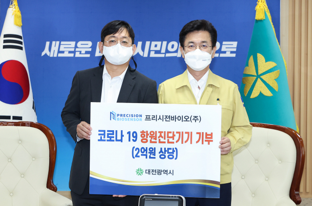 프리시젼바이오 김한신(사진 왼쪽) 대표이사가 허태정(″오른쪽) 대전시장에게 코로나19 항원진단기기를 기탁하고 있다. 사진제공=대전시