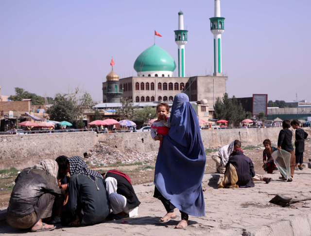 이슬람 무장세력 탈레반이 재장악한 아프가니스탄 수도 카불에서 4일(현지시간) 전신을 가린 부르카 차림의 한 여성이 아기를 안고 시내를 걸어가고 있다. /로이터연합뉴스