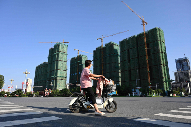 지난 14일 파산 위기에 몰린 중국의 대형 민영 부동산 기업 헝다 그룹이 허난성 주마뎬에서 진행하고 있는 아파트 건설 현장 앞으로 스쿠터를 탄 여성이 지나가고 있다. /연합뉴스