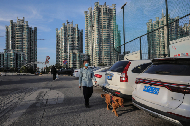 중국 베이징의 한 주거 지역에서 한 주민이 개를 산책시키며 주차된 차들 옆을 지나가고 있다. /EPA연합뉴스