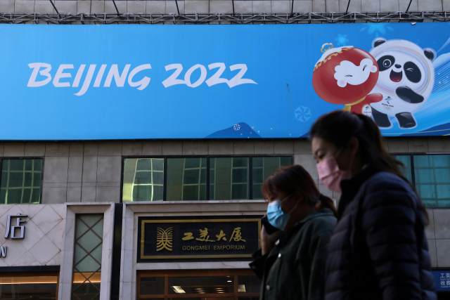 베이징 동계올림픽 100일을 앞둔 지난 27일 마스크를 쓴 베이징 시민들이 올림픽 홍보판 아래를 바쁘게 지나치고 있다. /로이터연합뉴스