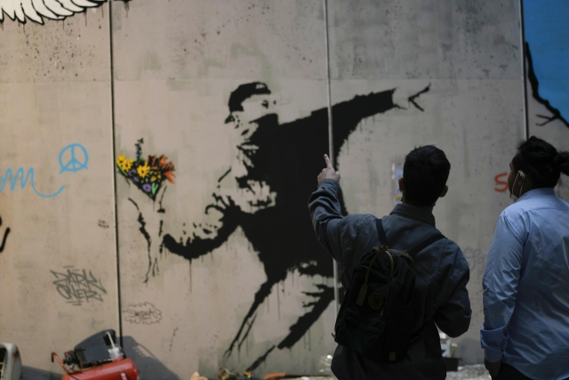 지난 2일(현지시간) 이탈리아 밀라노에서 열린 뱅크시 전시회 제막식에서 관람객들이 뱅크시의 작품 ‘사랑은 공중에’를 복제한 벽화를 관람하고 있다. /연합AP