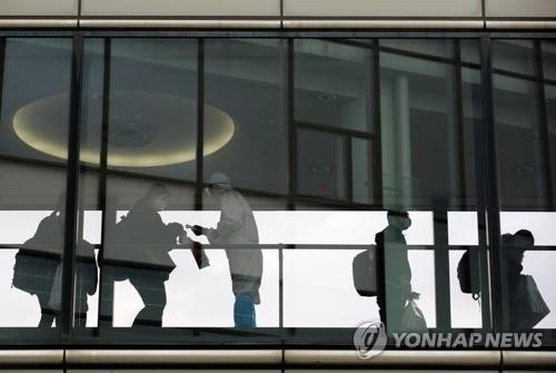 일본 수도권 관문인 나리타국제공항에서 코로나19 예방을 위해 방호복을 입은 공항 직원이 국제선 탑승객의 체온을 재고 있다./로이터연합뉴스