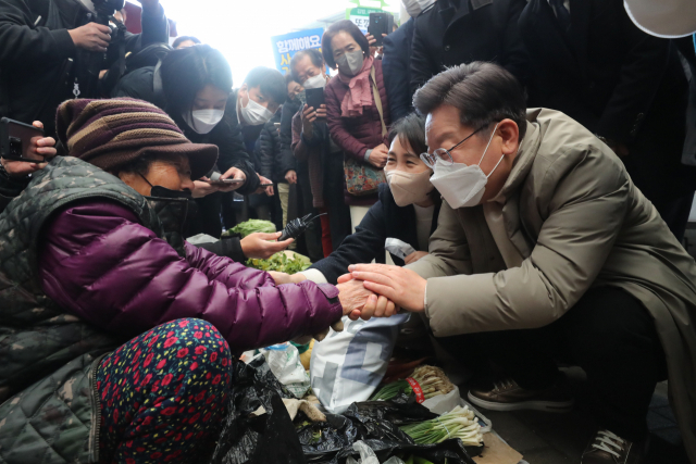 이재명(오른쪽) 더불어민주당 대선 후보 내외가 12일 경북 예천군 예천읍 상설 시장을 방문, 좌판에서 냉이를 사며 할머니의 손을 잡고 있다. /연합뉴스