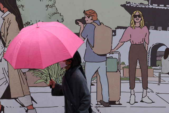 지난달 30일 서울 광화문광장 외벽에 그려진 여행객 그림 앞으로 한 시민이 우산을 쓰고 지나가고 있다. /연합뉴스