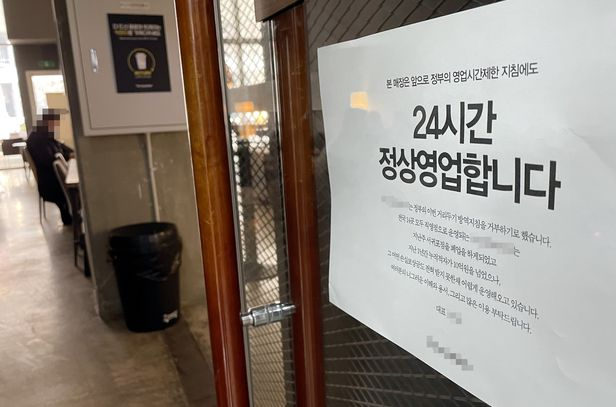 지난 21일 인천의 한 카페 출입문에 정부 영업제한 조치를 거부하고 24시간 영업을 강행한다는 내용의 안내문이 부착돼 있다. /연합뉴스