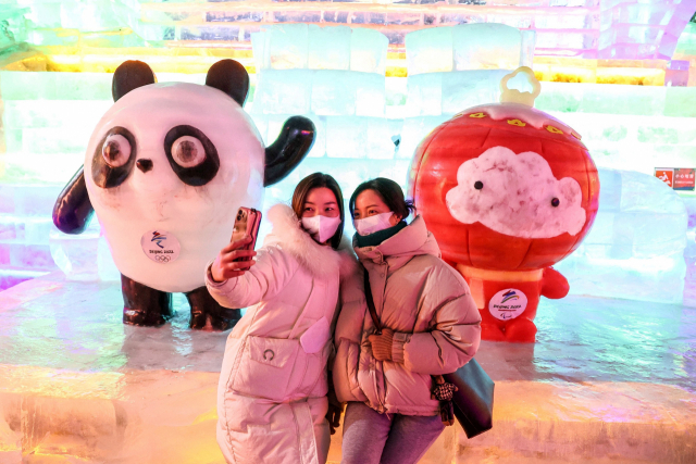 지난 12일 중국 베이징에서 두 여성이 베이징 동계올림픽 마스코트인 빙둔둔(왼쪽)과 쉐룽룽을 배경으로 셀카를 찍고 있다. /AFP연합뉴스