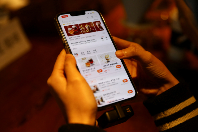 한 중국 기자가 18일 미디어 행사에서 메이투안 앱을 켜고 스타벅스 메뉴 주문을 시연해보고 있다. /로이터연합뉴스