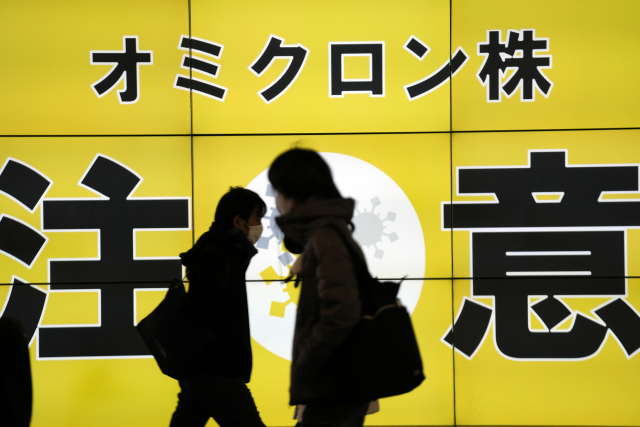 24일 일본 수도 도쿄 거리에서 마스크를 쓴 시민이 코로나19 오미크론 변이 확산에 주의하라는 내용의 공공 안내판 앞을 지나고 있다. /도쿄 AP=연합뉴스