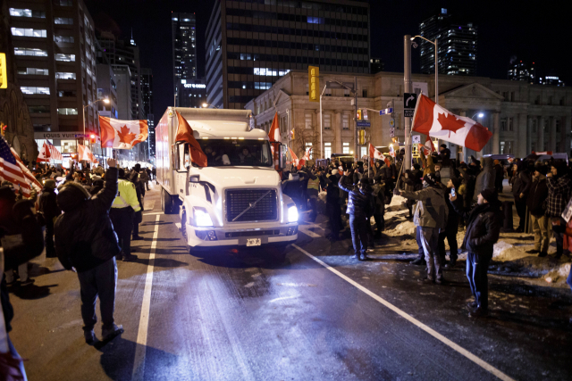 5일(현지 시간) 캐나다 오타와의 한 거리에 코로나19 백신 의무화를 반대하는 트럭 기사의 트럭이 들어서자 방역 정책 반대 시위대가 국기를 흔들며 환영하고 있다. AFP연합뉴스