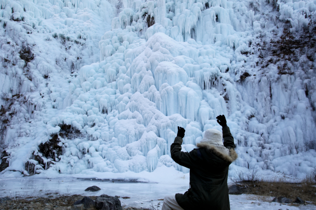 한 여행객이 빙벽을 기어오르는 듯한 포즈로 취하고 있다. 사진은 청송 아이스 클라이밍 경기장 빙벽.