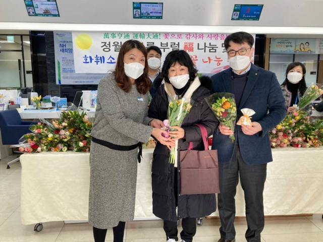 농협은행 창원시지부 로비에서 내방손님(중앙)에게 관계직원(좌우)이 꽃과 福부럼을 나눠준 뒤 기념 사진촬영을 하고 있다. /사진제공=경남농협