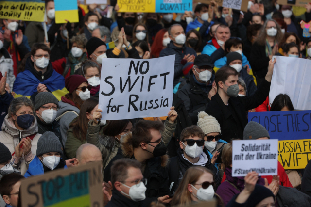 독일 프랑크푸르트 시내에서 26일(현지시간) 러시아의 우크라이나 침공을 규탄하는 시위가 벌어진 가운데 한 시위 참가자가 러시아 은행들을 국제은행간통신협회(SWIFT·스위프트) 결제망에서 배제할 것을 촉구하는 팻말을 들고 있다. /연합뉴스