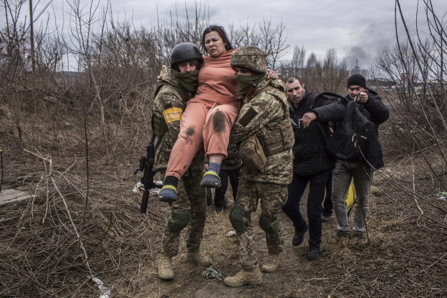 지난 6일(현지시간) 우크라이나의 수도 키이우 인근 소도시인 이르핀에서 우크라이나 군인들이 한 여성을 들고 간이 도로를 따라 이동하고 있다. 이날 러시아군이 이르핀에 포격을 시작하자, 많은 시민이 도시를 빠져나가고 있다. /AP 연합뉴스