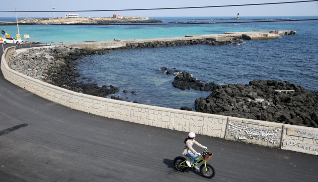 우도 해안 도로를 한 여행객 자전거를 타고 지나가고 있다. 그 뒤로 보이는 곳이 비양도다.