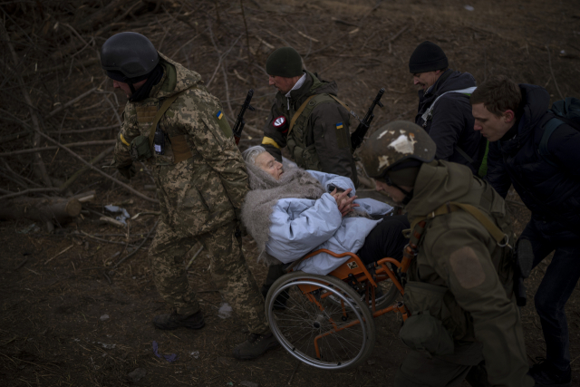 7일(현지시간) 우크라이나 수도 키이우(키예프) 외곽 소도시 이프린에서 포성이 울리는 가운데 우크라이나 군인들이 휠체어를 탄 노인의 피란을 돕고 있다. /연합뉴스