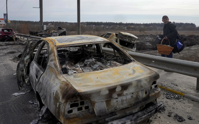 12일(현지 시간) 우크라이나 수도권인 키이우 북쪽 이르핀에서 한 주민이 폭탄에 맞아 불탄 뒤 곳곳에 널브러져 있는 차량 사이로 피란하고 있다. AP연합뉴스