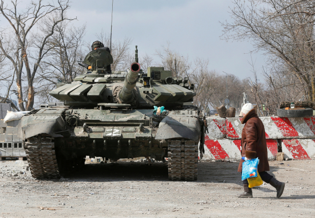 러시아군에 포위된 우크라이나 남부 항구 도시 마리우폴에서 18일(현지시간) 한 주민이 친러시아 민병대의 탱크 옆으로 지나가고 있다. /로이터연합뉴스